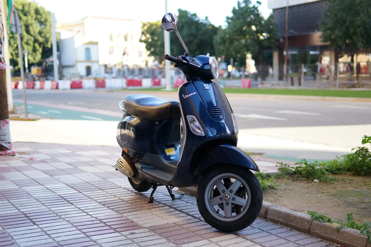 Donkerblauwe Vespa-scooter geparkeerd langs de straat
