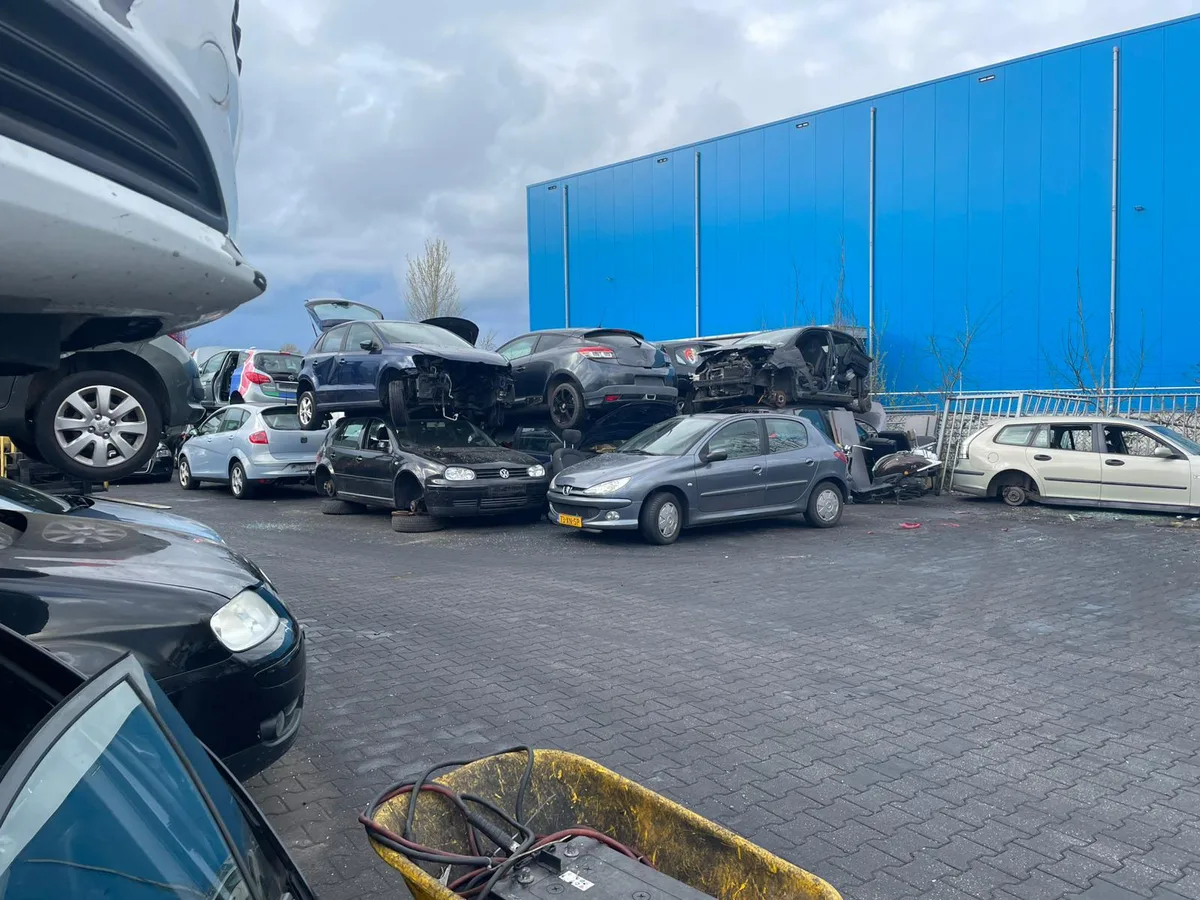 Autosloperij met gestapelde sloopauto's waaronder VW Golf en Peugeot